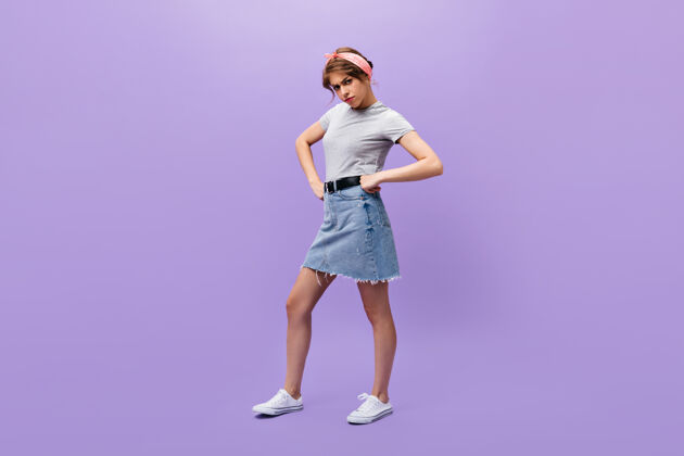 年轻穿着牛仔裙和灰色衬衫的严肃女人看着镜头不满意的女孩戴着夏天的头巾 穿着白色时髦的运动鞋摆姿势愤怒紫色头发