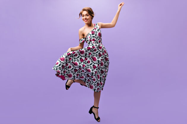 姿势快乐的女人穿着时髦的裙子在紫色的背景上跳跃快乐迷人的女孩穿着花式的时髦服装在孤立的背景上摆姿势花女孩微笑