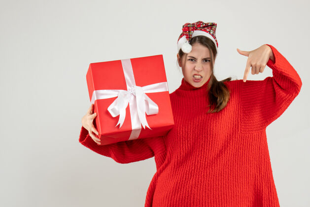 手指正面图愤怒的女孩戴着圣诞帽拿着礼物手指朝下站着惊喜愤怒的女孩盒子