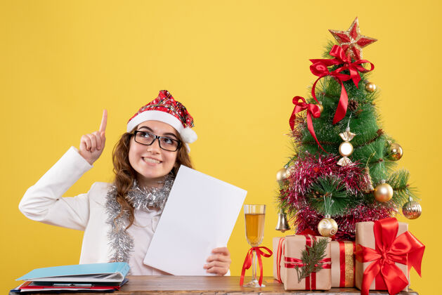 圣诞前视图女医生在她的桌子后面拿着文件庆祝一年圣诞树