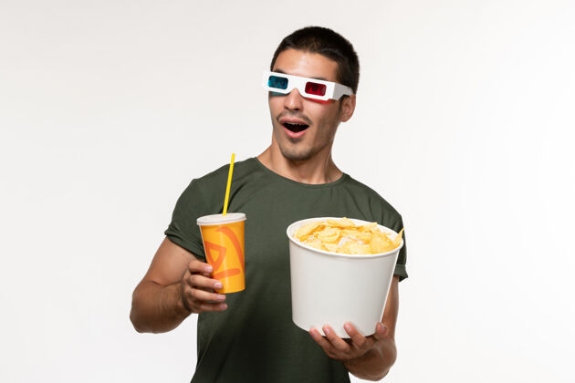玻璃正面图身穿绿色t恤的年轻男性手持土豆cips和戴着d墨镜的苏打水在白色墙纸上拍摄男性孤独电影咖啡早餐杯子