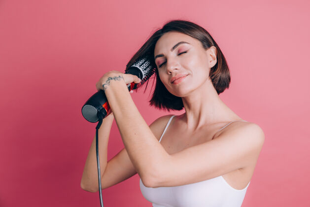 刷子粉色背景上的女人拿着圆刷吹风机来做发型肖像特写女士