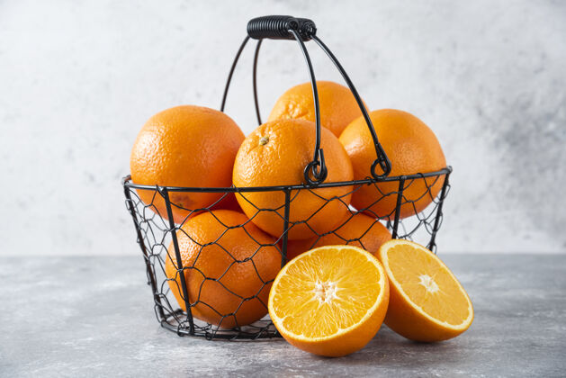 柑橘石桌上放着一个装满多汁橙子的金属黑色篮子异国情调成熟天然