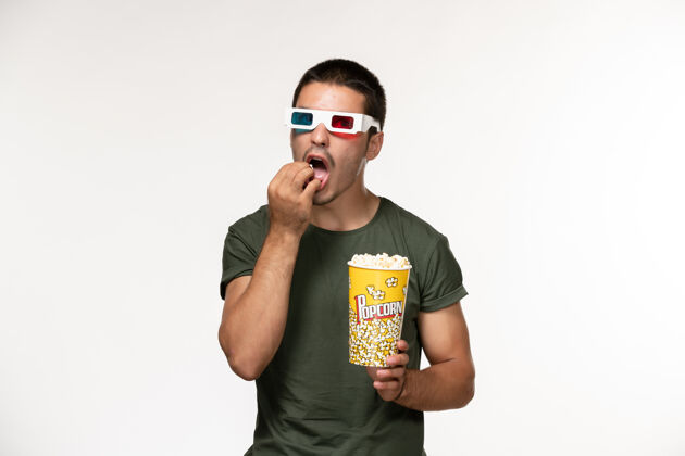 男人正面图身穿绿色t恤的年轻男性手持爆米花戴着d墨镜在白墙上吃电影孤独电影院男性电影观点电影成人