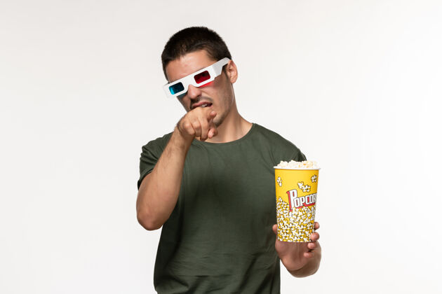 年轻男性正面图身穿绿色t恤的年轻男子戴着d型太阳镜拿着爆米花在白墙上看电影孤独电影院成人观看爆米花