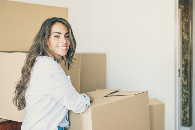 搬迁一位快乐美丽的西班牙年轻女子站在成堆的纸箱旁 在她的新公寓里打开东西人房间女人