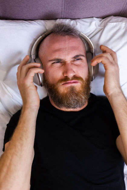 周末快乐的白人男子戴着耳机躺在床上听他最喜欢的音乐 独自休息 跳舞在线包装房子