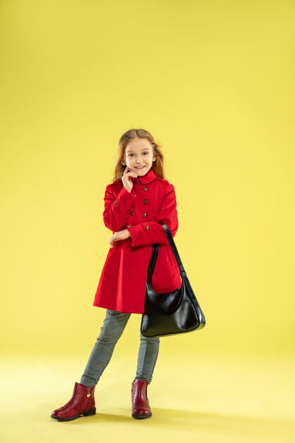 衣服一个穿着红色雨衣 手里拿着一个黄底黑包的时髦白人女孩的完整肖像室内可爱靴子