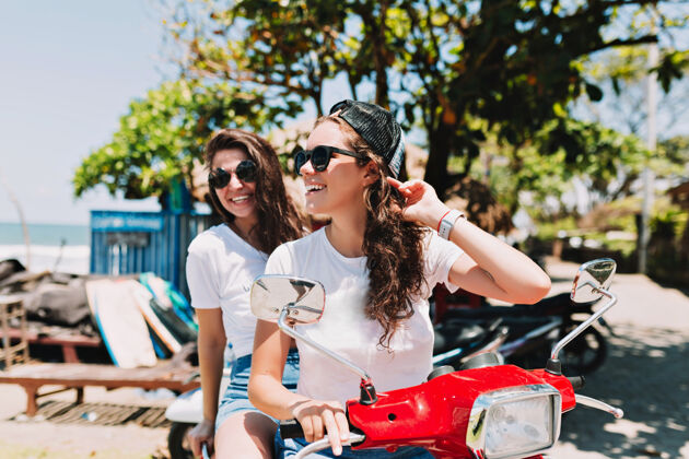 活动户外写真两位年轻漂亮的女子穿着白色t恤 戴着墨镜 在阳光下环岛流淌 玩得很开心 她们微笑着交谈着年轻人家庭欢呼