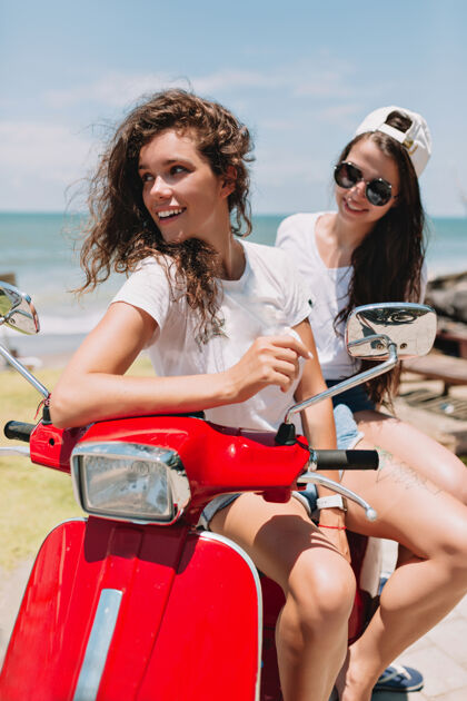 时尚令人难以置信的两个快乐的女人在阳光下骑着红色的摩托车在海边和大自然的小岛上游玩 真正的快乐情感 旅行 旅行 快乐的情感二女人自行车