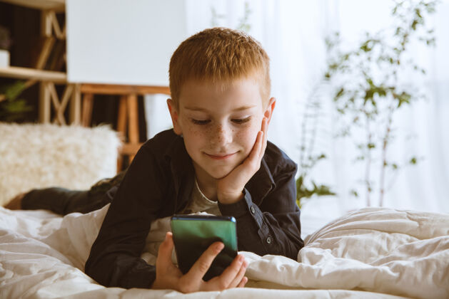娱乐男孩在家里使用不同的小玩意小模型智能手表 智能手机或平板电脑和耳机反应游戏人