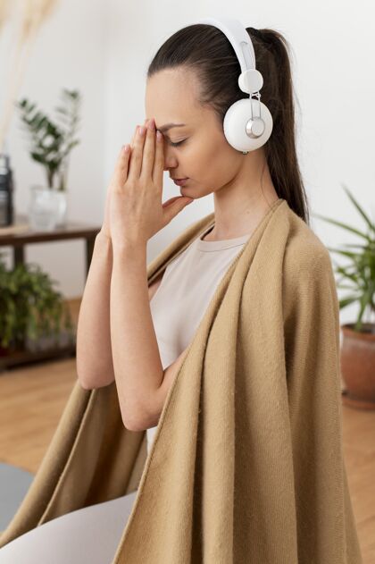 侧视戴着耳机在家冥想的女人瑜伽毯子技术