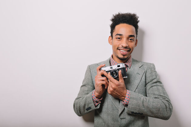 男人室内写真的快乐的非裔美国男性穿着灰色夹克手持相机在灰色的手上时尚表情欢呼