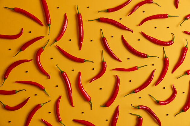 胡椒头顶上拍摄的长长的 薄薄的 成熟的红辣椒和黑胡椒 围绕着黄色的工作室墙壁食物背景一套辣椒各种香料蔬菜和营养概念明亮配料品种
