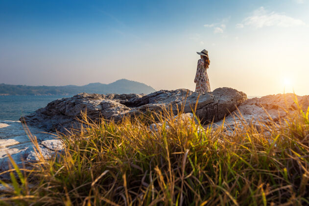 亚洲夕阳下站在四长岛岩石顶上的年轻女子背包岛屿冒险