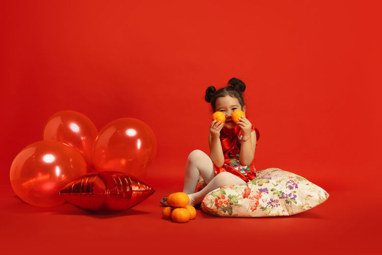 中文气球和普通话的心情摆可爱的姿势亚洲可爱的小女孩隔离在传统服装的红墙庆祝活动 人类的情感 节日复制空间美丽文化祝福