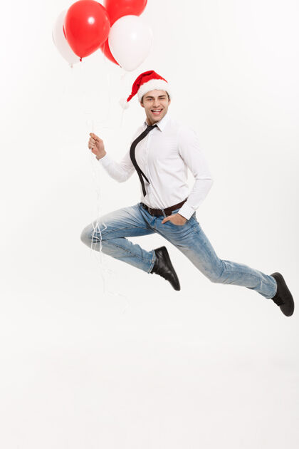 飞行英俊的商人戴着红气球的圣诞帽跳起来庆祝圣诞快乐乐趣享受圣诞老人