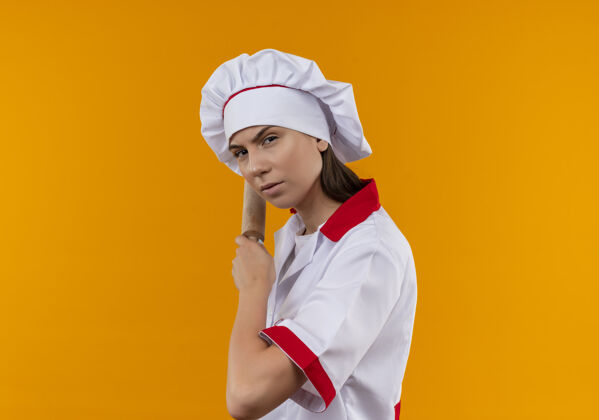 空间穿着厨师制服的年轻严肃的白人厨师女孩站在一边 拿着擀面杖在后面的橘子上 留着复印空间持有严肃侧