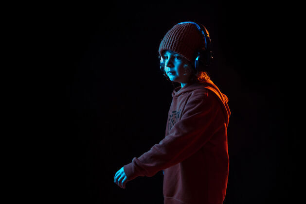 平板电脑听音乐和跳舞霓虹灯下黑暗墙上的白人男孩肖像美丽的卷曲模型人类情感的概念 面部表情 销售 广告 现代科技 小玩意男孩颜色显示