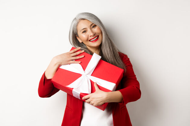 盒子快乐的亚洲祖母拥抱着红色的礼盒 微笑着感激 感谢礼物 站在白色的背景下亚洲人信心关系