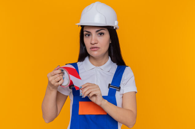 粘合剂穿着施工制服和安全帽的年轻建筑工人年轻建筑胶带