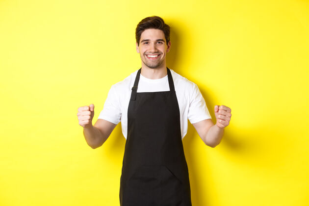 自信友好的咖啡店服务员举手站立 放置您的标志或徽标 站在黄色背景上黄色厨师时尚