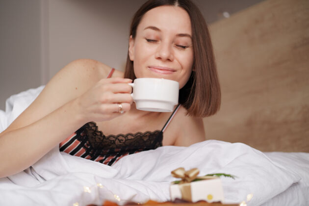 咖啡女人在床上醒来 拿着礼物和咖啡 旁边站着棉花糖床礼物浪漫