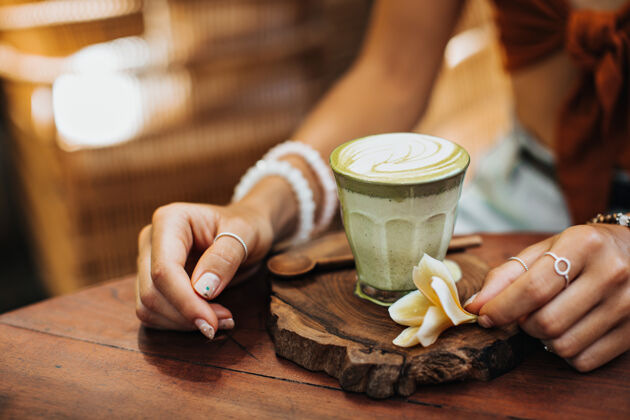土地晒黑的女人坐在咖啡馆里摆出一杯抹茶加牛奶的姿势美丽热茶