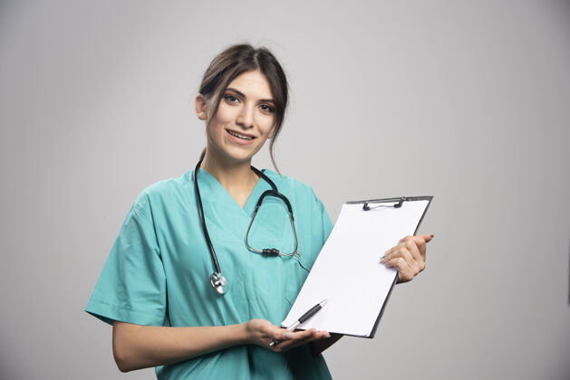 工作年轻的女医生拿着灰色的剪贴板女性医生听诊器