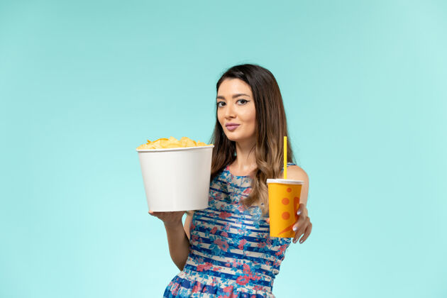 女性正面图年轻的女性拿着篮子和薯片 在蓝色的表面上喝酒举行年轻的女性薯片