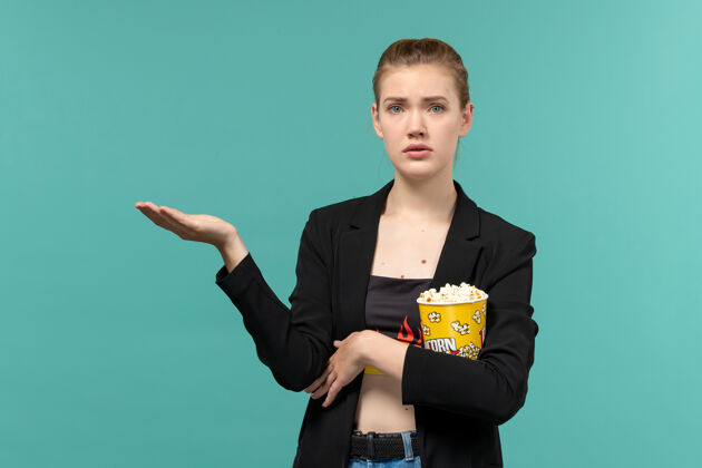 爆米花前视图年轻女性手持爆米花包在浅蓝色表面看电影抱男电影