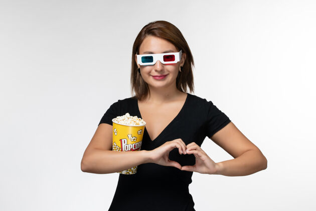 孤独正面图戴着d型太阳镜拿着爆米花的年轻女性在浅白的表面上看电影抱着年轻女性电影院