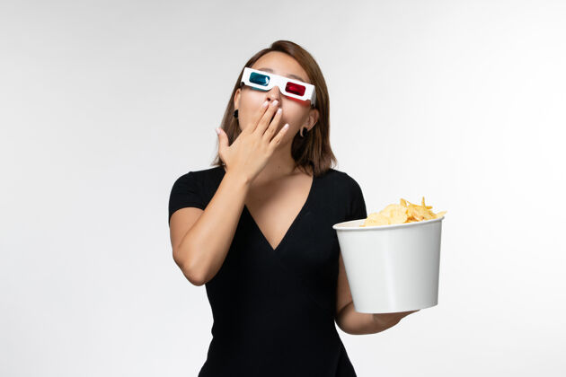 年轻女性正面图年轻女性戴着d型太阳镜拿着薯片 在白色表面看电影打呵欠土豆打哈欠太阳镜