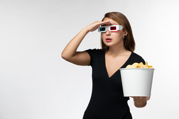 看正面图年轻女性戴着d型太阳镜拿着薯片 在浅白的表面上看电影抱电影前面