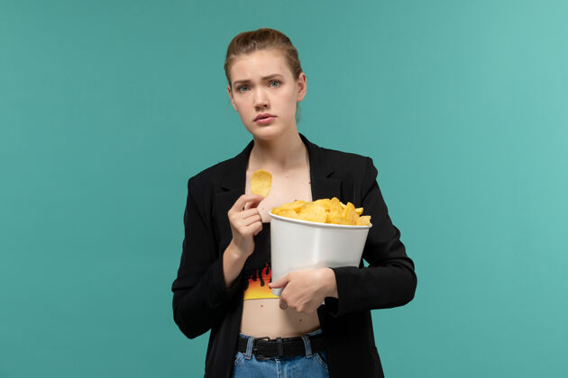 情侣前视图年轻女性拿着和吃薯片在浅蓝色的表面上看电影服务员前面浅蓝色