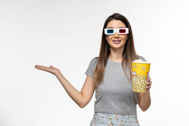 电影正面图：年轻女性手持爆米花 戴着d型太阳镜在浅白的表面上看电影前面太阳镜看