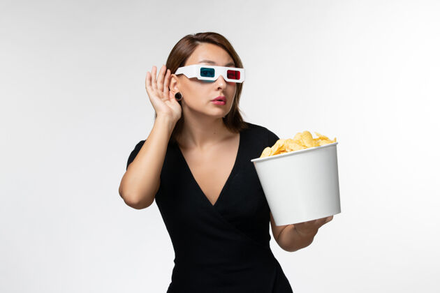 电影院正面图年轻女性戴着d型太阳镜拿着薯片 试图在白色表面上听到声音美丽前面电影