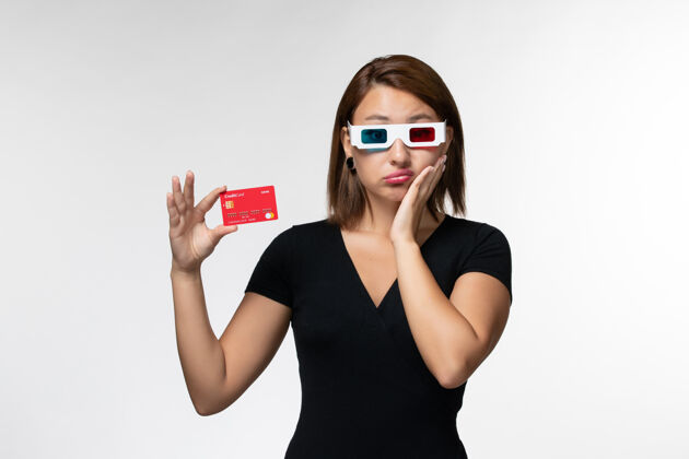 银行正面图年轻女性手持红色银行卡 戴着d型太阳镜 白色表面电影举行美丽