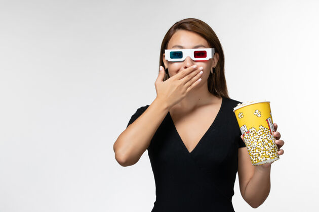 爆米花正面图戴着d型太阳镜拿着爆米花的年轻女性在白色表面看电影太阳镜美丽电影