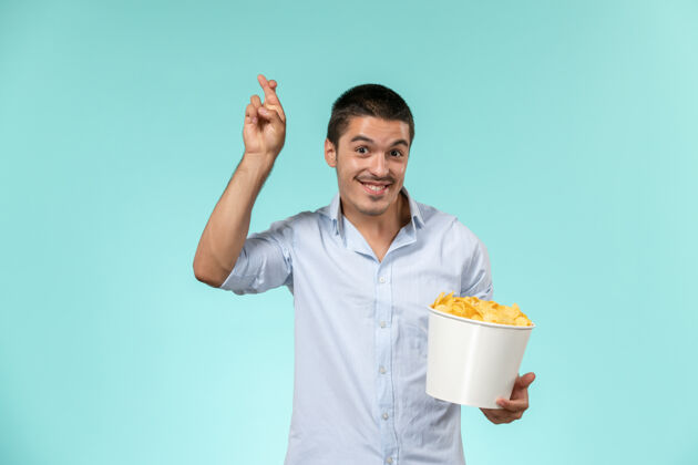 抱着正面图：年轻的男性拿着土豆片篮子 微笑着站在蓝色的水面上剧院电影院篮子