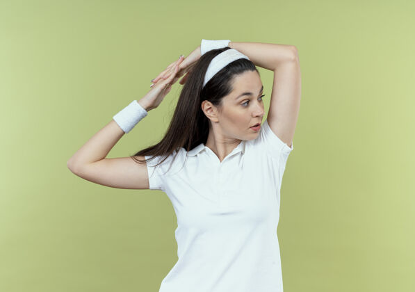 靠边戴着头巾的年轻健身女士站在轻薄的墙壁上 向一边望去 伸出双手站立年轻头带