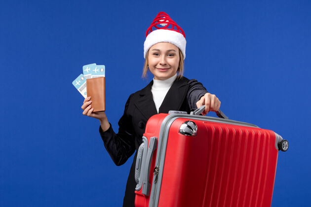 圣诞节正面图：年轻女子拿着蓝色背景的机票包度假工作包举行