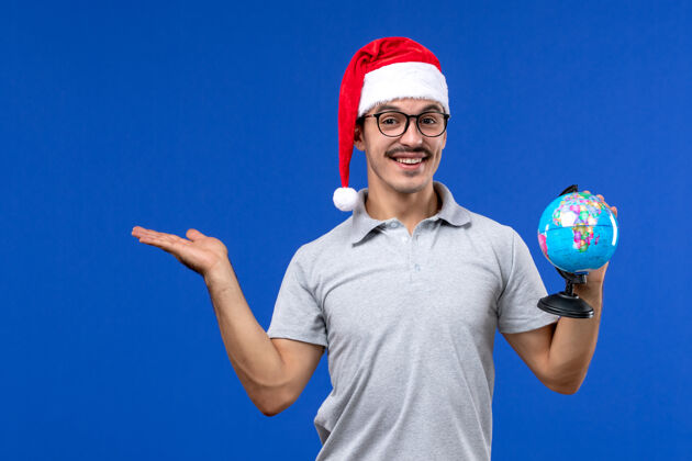人正面图：年轻男子手持地球仪在蓝墙飞机上人类度假之旅圣诞节年轻男性飞机