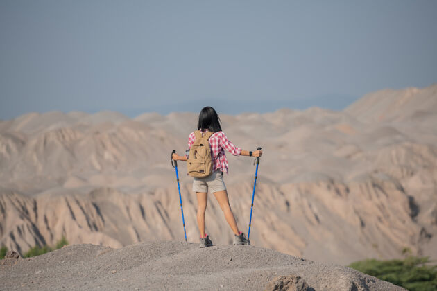 极点适合年轻女子徒步在山上站在岩石山顶山脊与背包和杆眺望风景太阳悬崖极限