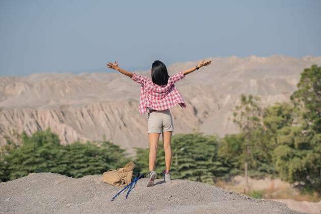 女孩适合年轻女子徒步在山上站在岩石山顶山脊与背包和杆眺望风景小径运动散步