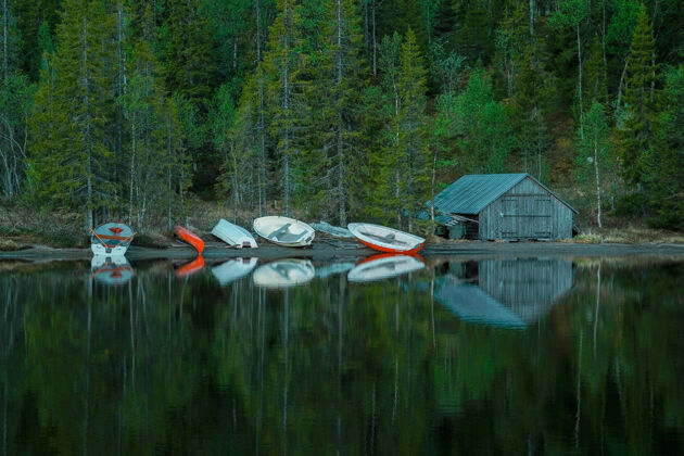 度假小木屋 旁边是平静的湖岸上的小船 前面是一片绿色的森林树休闲宁静