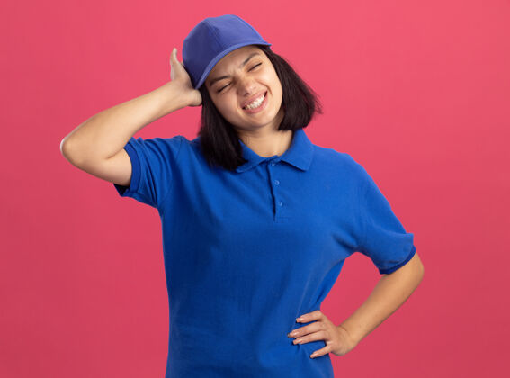 女孩一个穿着蓝色制服 戴着帽子 站在粉红色的墙上头痛的年轻送货员 很不高兴不高兴头痛年轻