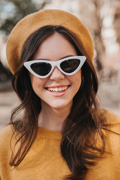 贝雷帽戴着黄色贝雷帽和太阳镜的微笑女孩的特写照片穿着橙色毛衣的黑发年轻女子边走边笑花春天健康