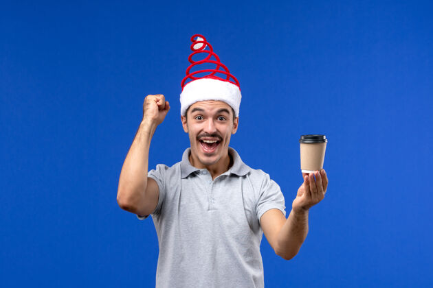 年轻男性正面图年轻男性拿着咖啡杯站在蓝色的墙上新年男性节日感慨圣诞节人光