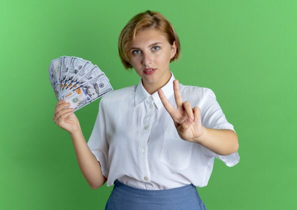 空间年轻自信的俄罗斯金发女孩拿着钱 用两个手指在绿色的空间里做手势绿色俄罗斯二
